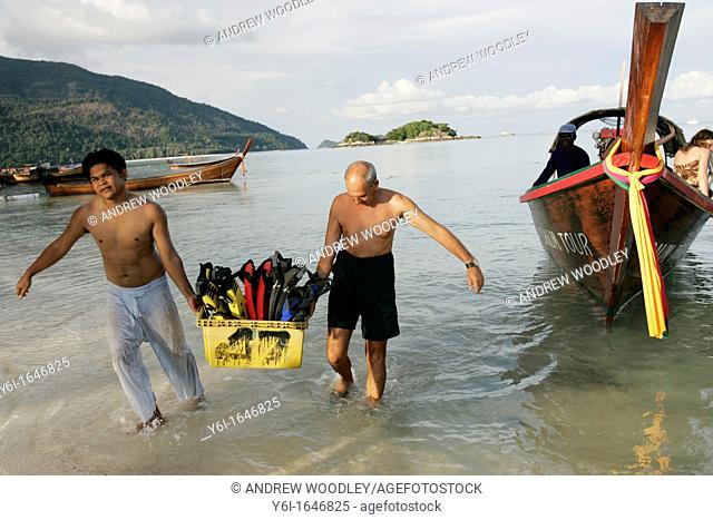 Men carry ashore diving equipment from traditional longtail boat Ko Lipe island Thailand