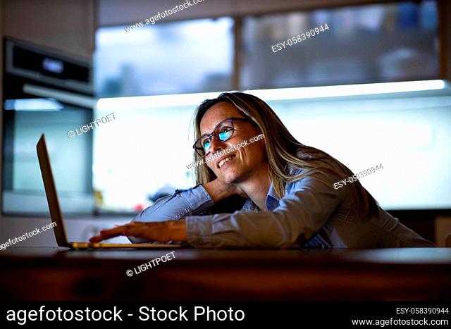 Middle-aged woman working late in the day on a laptop computer at home, running a business from home/working remotely for a corporation