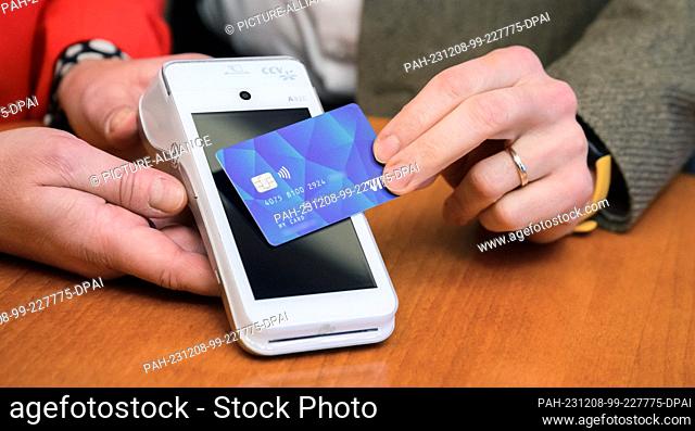 08 December 2023, Lower Saxony, Hanover: A VISA debit card is held in front of a reader at a press conference in Hanover City Hall