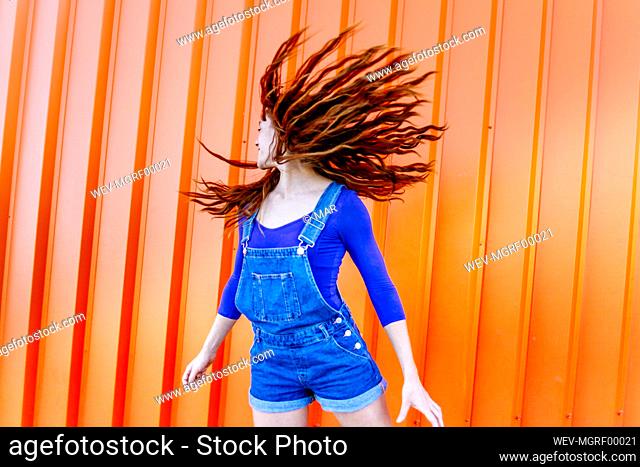 Playful woman tossing hair while standing against orange wall