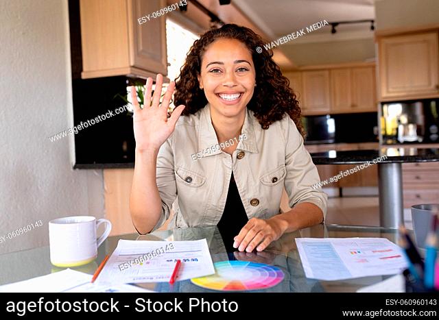 Portrait of smiling multiracial female freelancer waving on during video call at home office