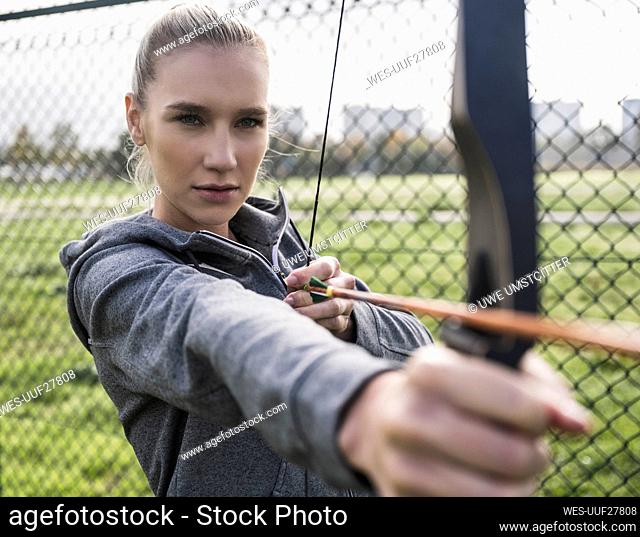 Confident sportswoman doing archery by fence