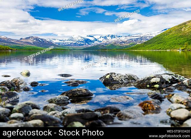 Norway, Innlandet, Rocky lakeshore in Jotunheimen National Park with mountains in background
