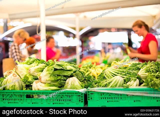 Farmers#39; food market stall with variety of organic vegetable. Vendor serving and chating with customers