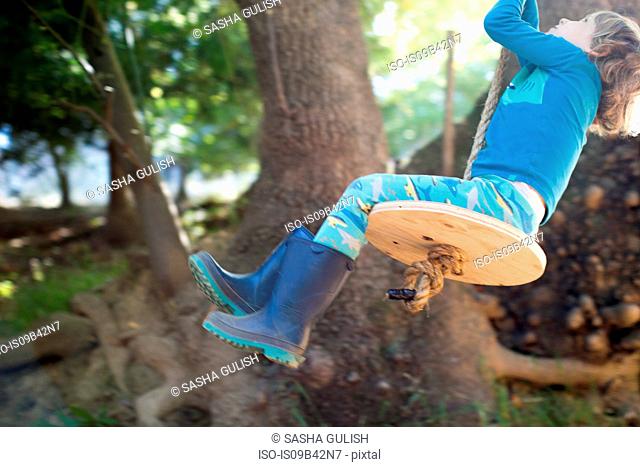 Young boy outdoors, swinging on rope swing