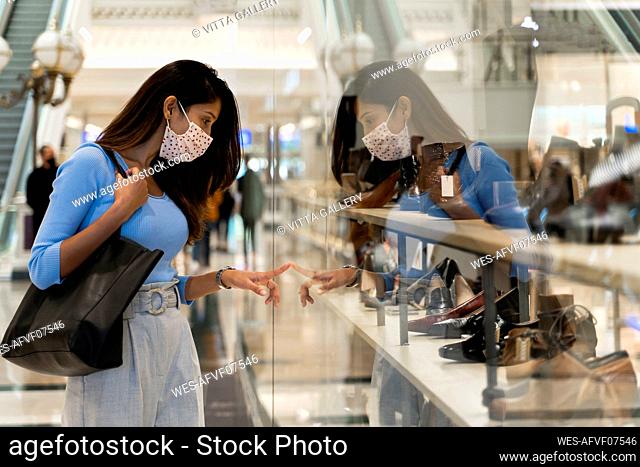 Woman wearing protective face mask while looking at footwear in shopping mall
