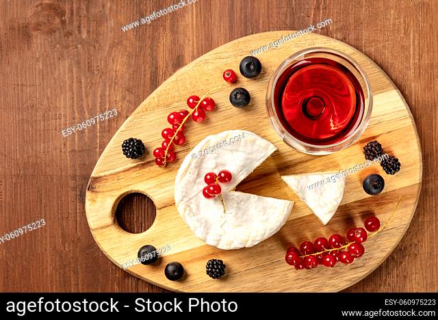 An overhead photo of Camembert cheese with a glass of red wine and fruits, on a dark rustic background with copy space
