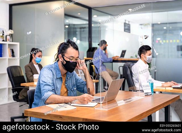 Group of interracial business worker team wear protective face mask in new normal office with social distance practice with hand sanitiser alcohol gel on table...