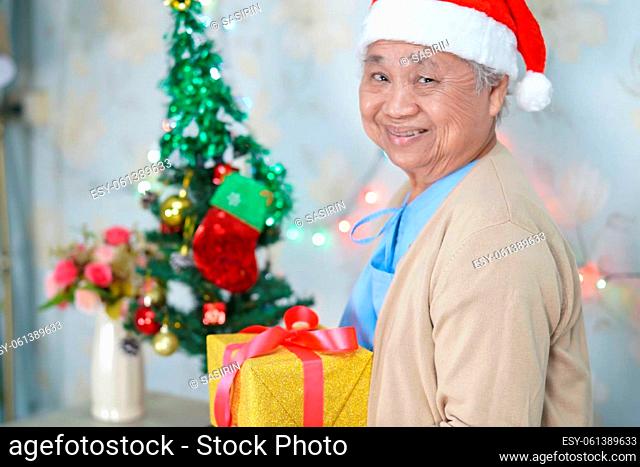 Asian senior or elderly old lady woman patient with Santa Claus helper hat holding gift box in Christmas and new year celebration festival holiday party in...