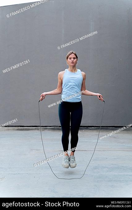Young woman skipping rope while standing against wall