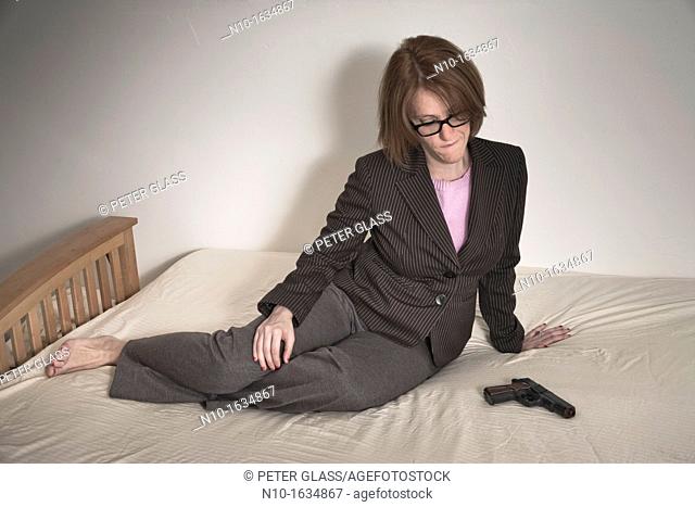 Woman sitting on her bed, next to a handgun