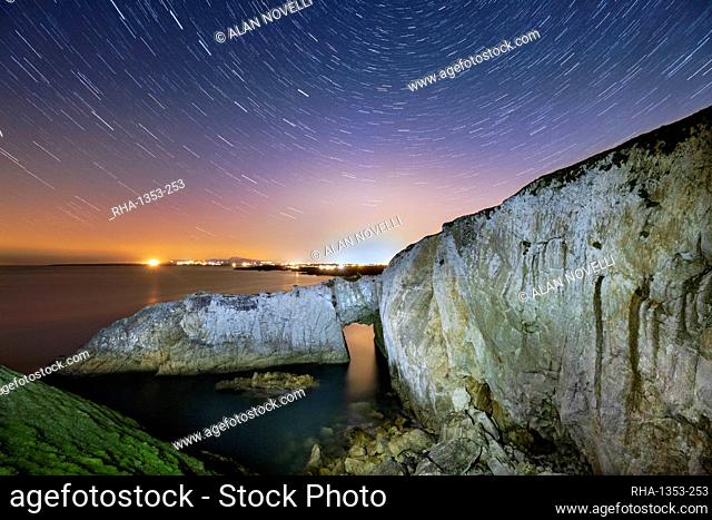 Star trails and night sky over Bwa Gwyn or the White Arch, near Rhoscolyn, Anglesey, North Wales, United Kingdom, Europe