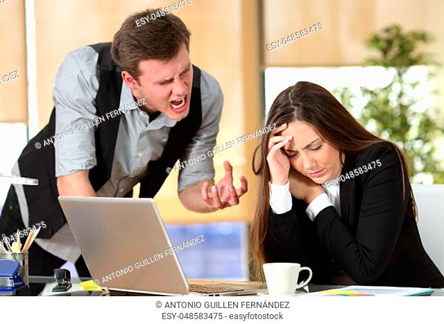 Bullying with an out of control boss shouting to a stressed employee in a desktop at office interior