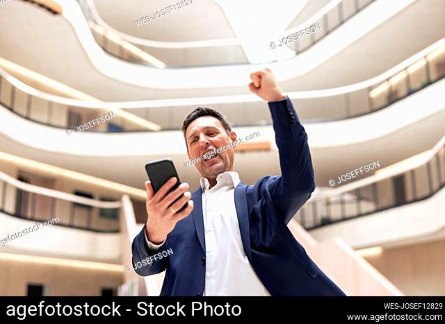 Happy businessman using mobile phone in lobby