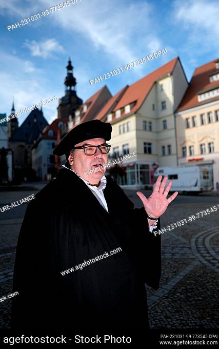 31 October 2023, Saxony-Anhalt, Lutherstadt Eisleben: Dirk Wellmitz, city guide in the role of Martin Luther, speaks to tourists on the market square