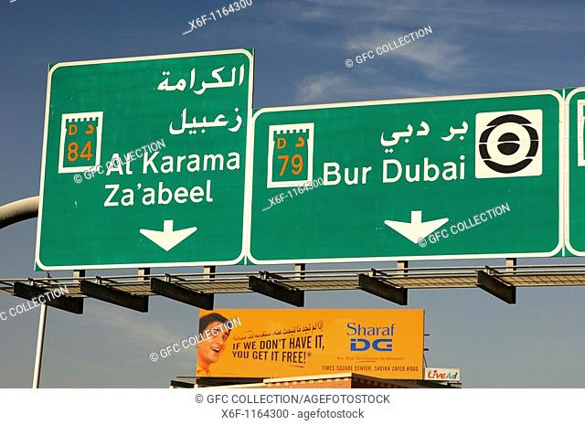 Directional road signs in English and Arabic and publicity board above the multi-lane roads in Dubai, United Arab Emirates