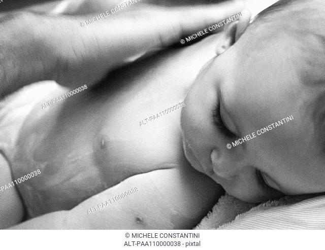 Adult hand rubbing lotion into baby's chest, close-up, b&w