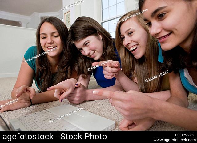 Four teenage girls using a laptop and pointing at the screen while laughing