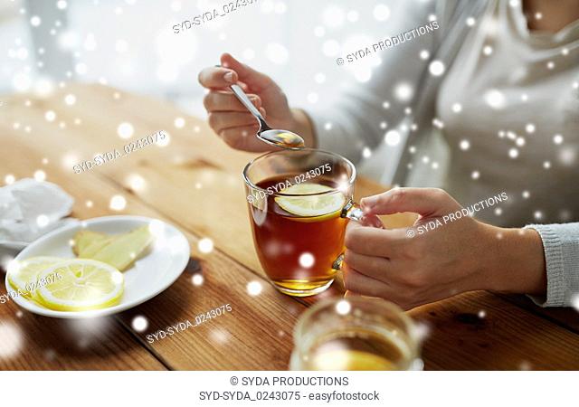 close up of woman adding honey to tea with lemon