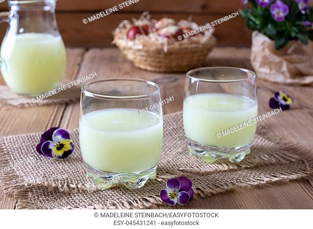 Fresh whey in two glasses and a jug, with pansy flowers in the background