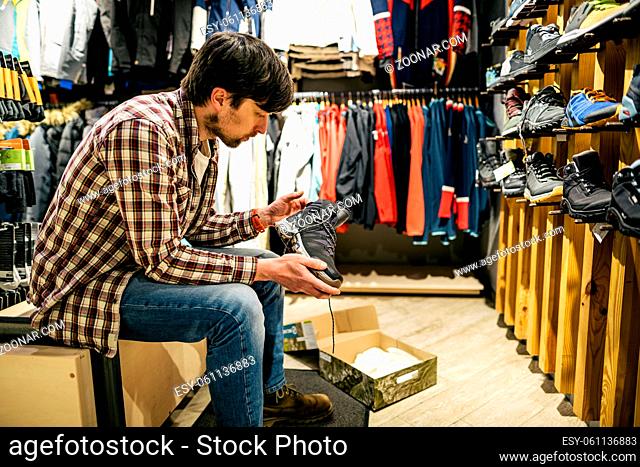 Man shopping in an outdoor store. Male buying mountain boots. Shopper in sports store select hiking shoes. Customer purchase of footwear for adventures