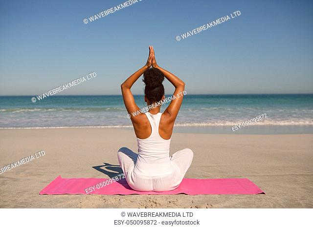 Rear view of African american woman doing yoga on exercise mat at beach in the sunshine
