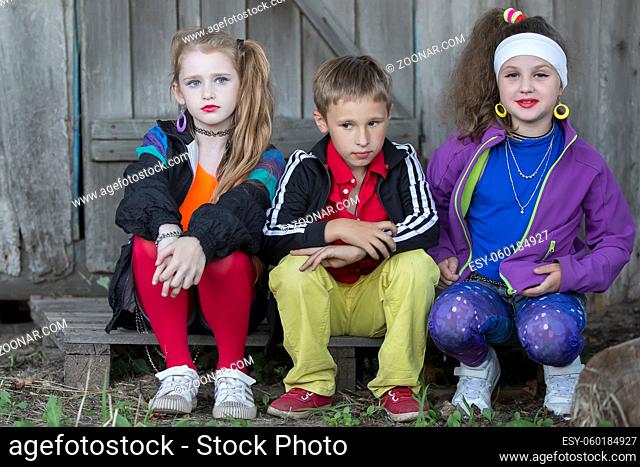 Funny children with bright make-up in krack clothes. A boy and two girls of school age are sitting on a wooden porch