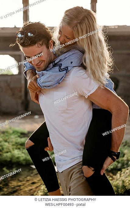 Happy young man giving girlfriend a piggyback ride in an old hall
