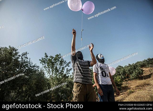 08 May 2021, Palestinian Territories, Juhor ad-Dik: Masked supporters of the Islamic Jihad Movement in Palestine release balloons filled with refrigerant gas...