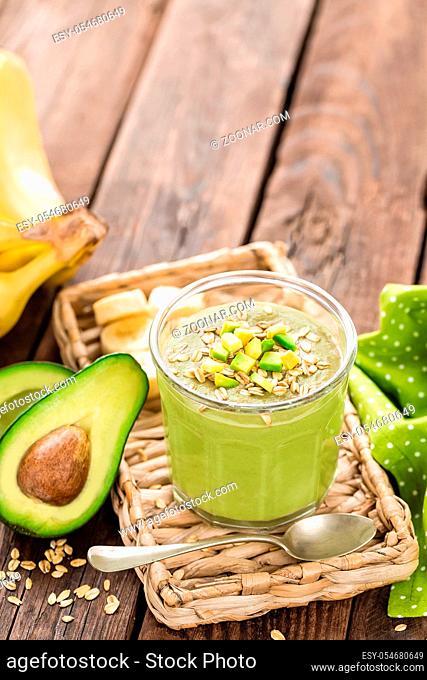 Avocado and banana smoothie with oats with ingredients in glass jar on wooden background, healthy eating