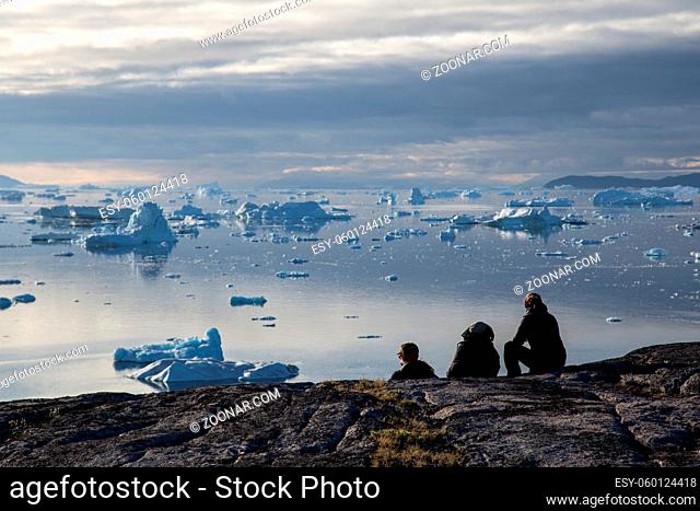 Rodebay, Greenland - July 09, 2018: A group of people sitting and looking at icebergs. Rodebay, also known as Oqaatsut is a fishing settlement north of...