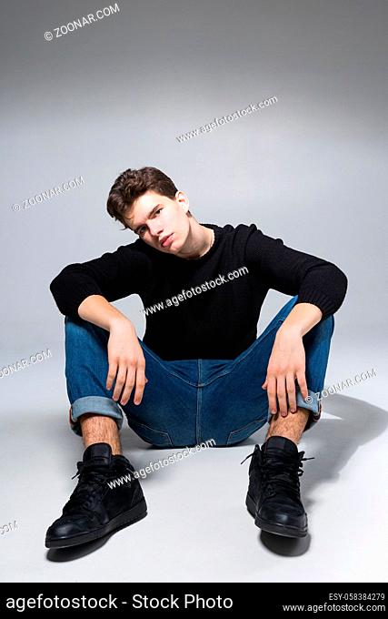 Stylish handsome man posing sitting on floor. Handsome Guy. cool fashion male model sitting on grey background and looking at the camera