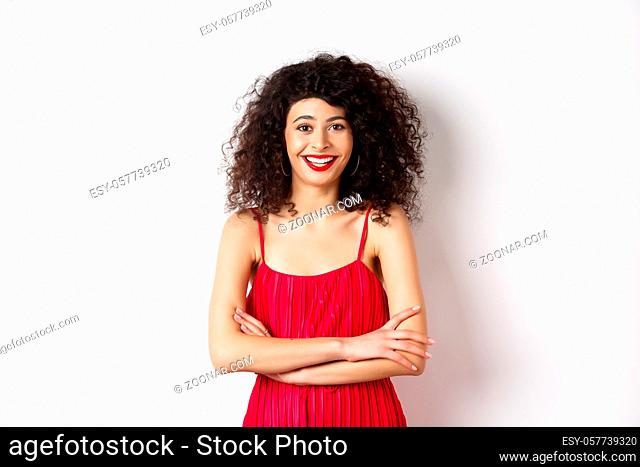 Elegant young woman in red dress with makeup, dressed-up for festive event, smiling happy at camera, standing over white background