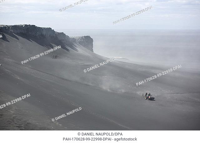 A truck with a trailer on which tourists are being transported stands on a sandy area in front of the Island of IngÃ³lfshöfði, Iceland, 27 June 2017