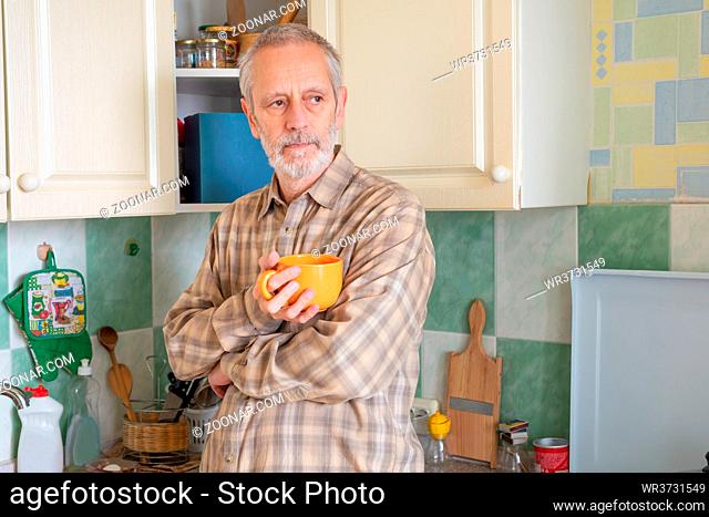 Mature man drinking his coffee in an orange cup, at morning in kitchen