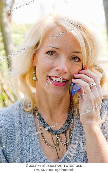 Portrait of a 44 year old blond woman talking on a mobile phone, outdoors
