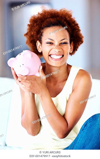 Excited African American woman sitting on sofa holding piggy bank