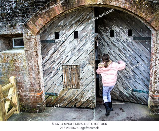 Preteen caucasian girl trying to push an old wood heavy door in an old Fort. Fort Macon State Park, originally called, Fort Dobbs then Fort Macon Military...