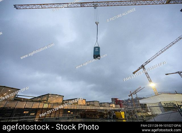 28 November 2023, Baden-Württemberg, Stuttgart: A mobile toilet cubicle is delivered by crane to the roof of the new railroad station as part of the...