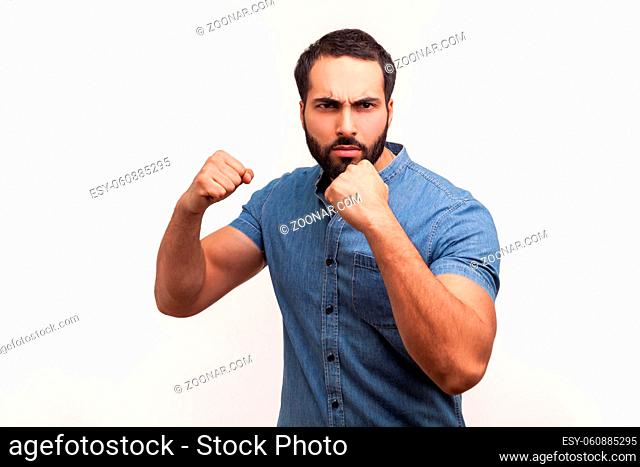 Athletic aggressive man fighter with beard holding clenched fists up ready to boxing, martial art trainer, self defense. Indoor studio shot isolated on white...