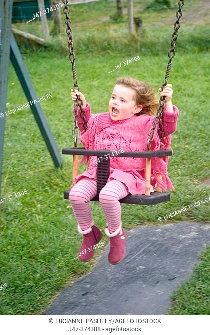Three year old girl swinging in the park all dressed in pink laughing