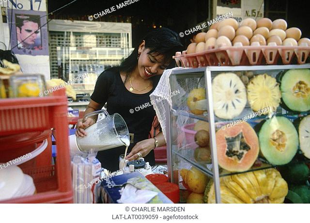 Young woman pouring drink. Fruit juice stall. Cut papaya. Melon. Pineapple. Eggs on tray