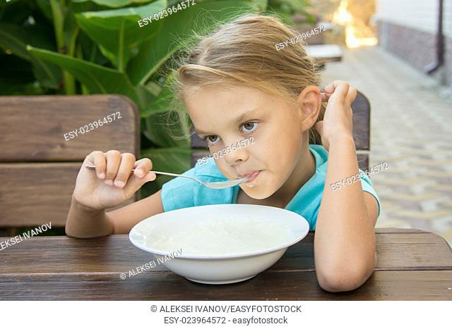 Six-year girl sitting at a table with a sour face and did not want to eat porridge for breakfast