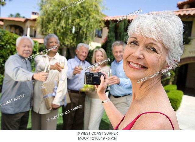 Senior woman photographing friends in garden while raising toast