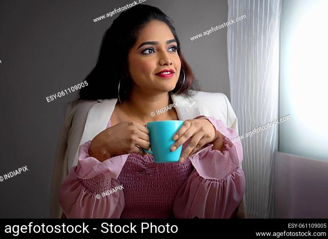Young Business woman sitting in office and looking outside with holding a cup of coffee