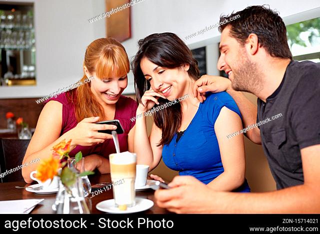Drei lachende Freunde mit Handys im Café