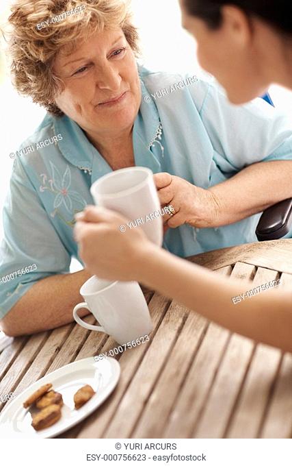 Happy old female patient having a cup of coffee with a nurse
