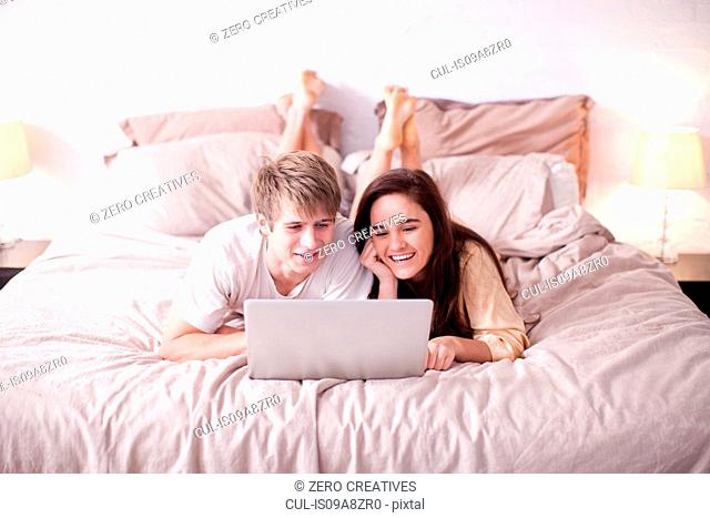 Young couple lying on bed watching laptop
