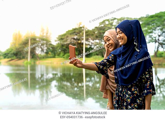 Young adult teenager Muslim Islamic Thai Asian women university students using smartphones to make thier selfie photographing