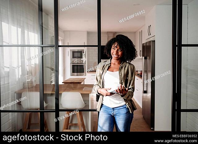 Contemplative woman with tablet PC leaning on sliding door at home